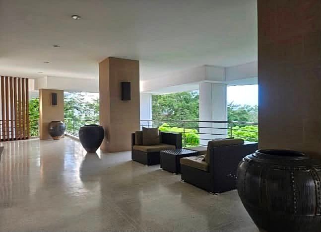 Hotel lobby lounge with dark sofa chairs and a small table, large black ceramic pots, and a view of greenery outside through open railings.