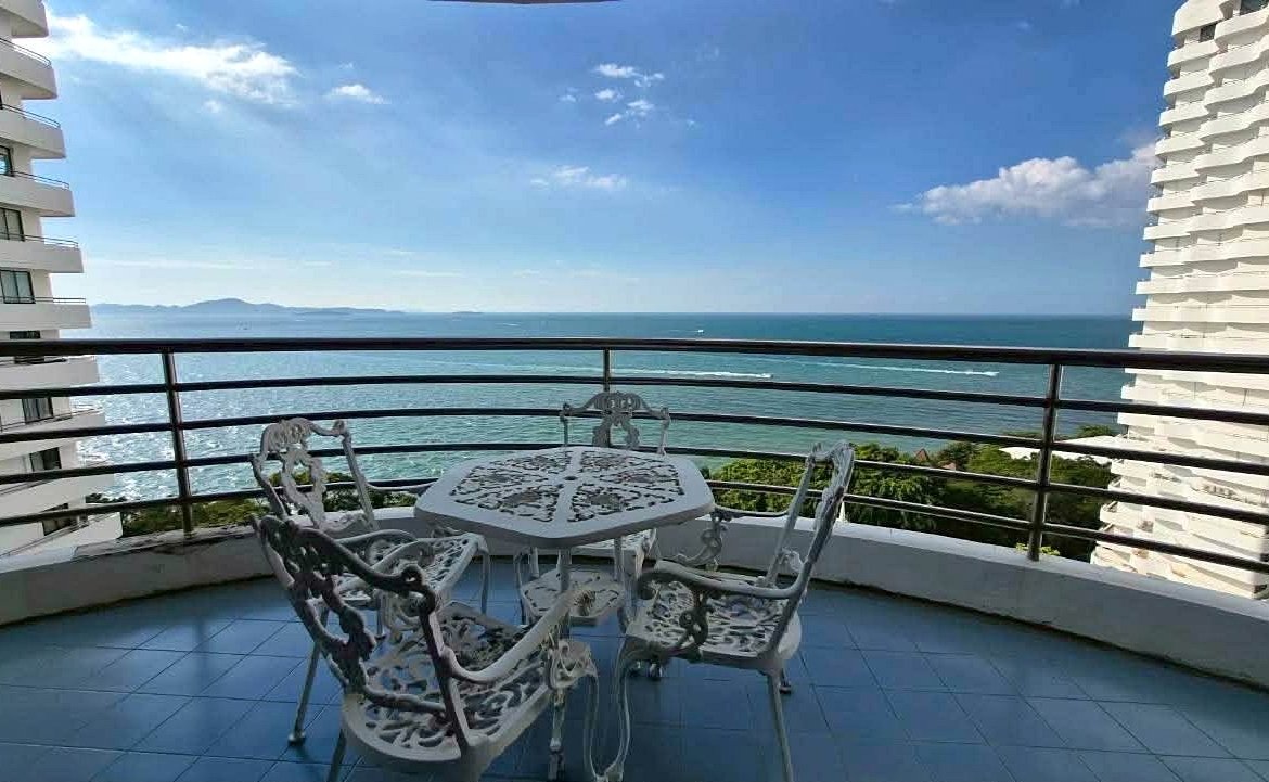White ornate metal table and four matching chairs on a curved balcony, overlooking the blue ocean and distant islands with a clear sky.