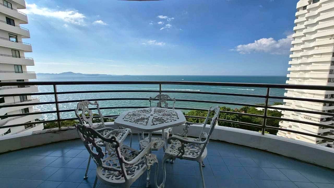 Royal_Cliff_Garden_Pattaya_Dlc639_2 White ornate metal table and four matching chairs on a curved balcony, overlooking the blue ocean and distant islands with a clear sky.
