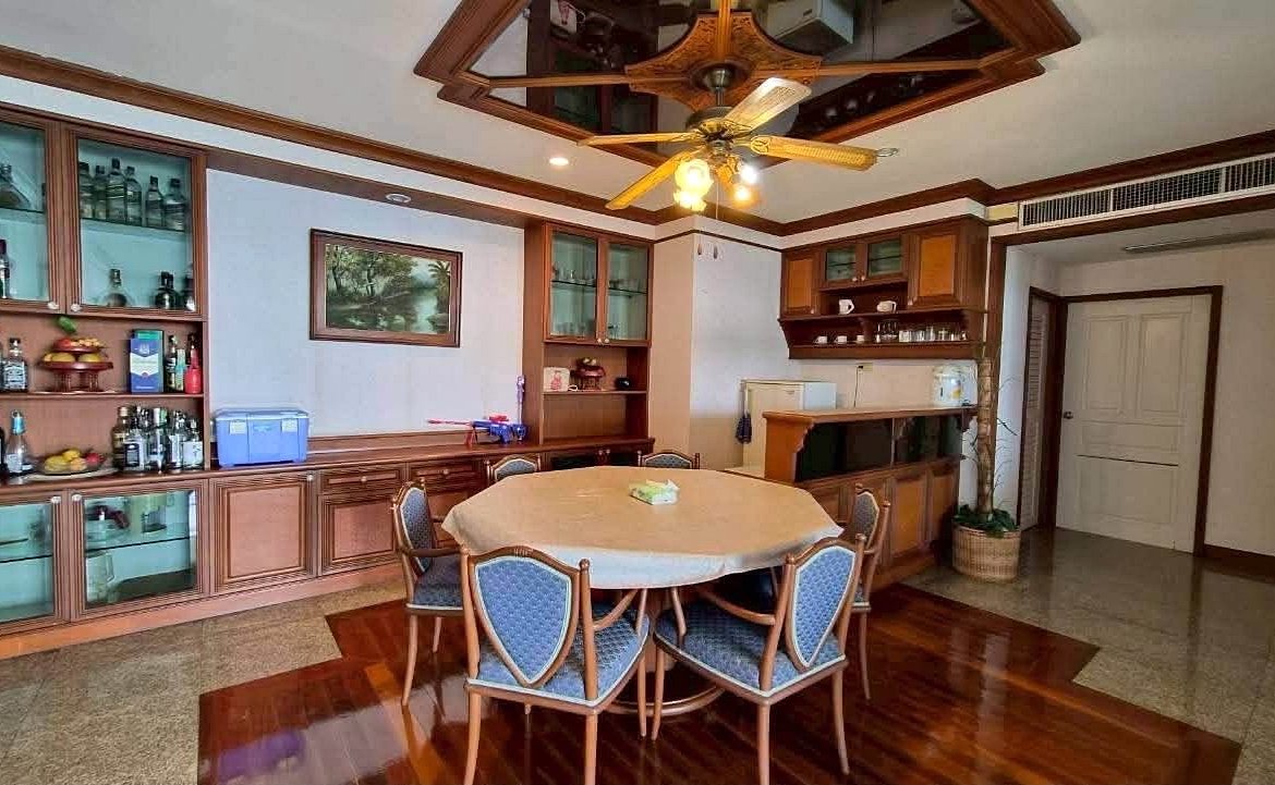 Round dining table with a beige tablecloth and blue-upholstered chairs in a wood-paneled dining room with a ceiling fan above