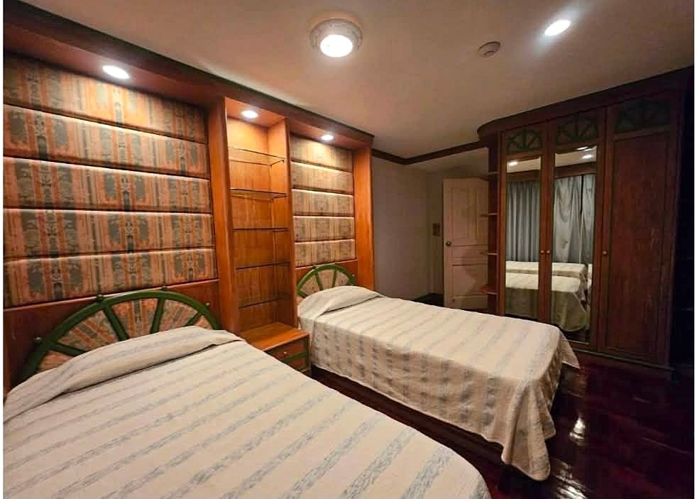 Hotel room with two single beds, striped bedspreads, and dark wood furniture including built-in shelves and a large mirrored wardrobe on the right.