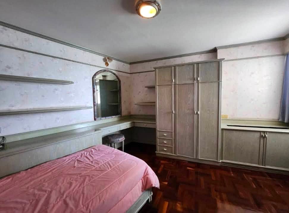 Bedroom with built-in gray wardrobes, shelves, and a pink bedspread on a low bed, parquet floor, and an arched doorway to a vanity area.