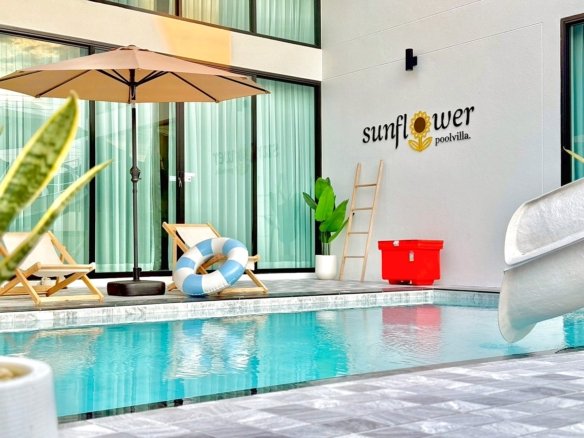 Poolside area at Sunflower Pool Villa two wooden lounge chairs a beige umbrella lifebuoy and a red cooler against a light wall