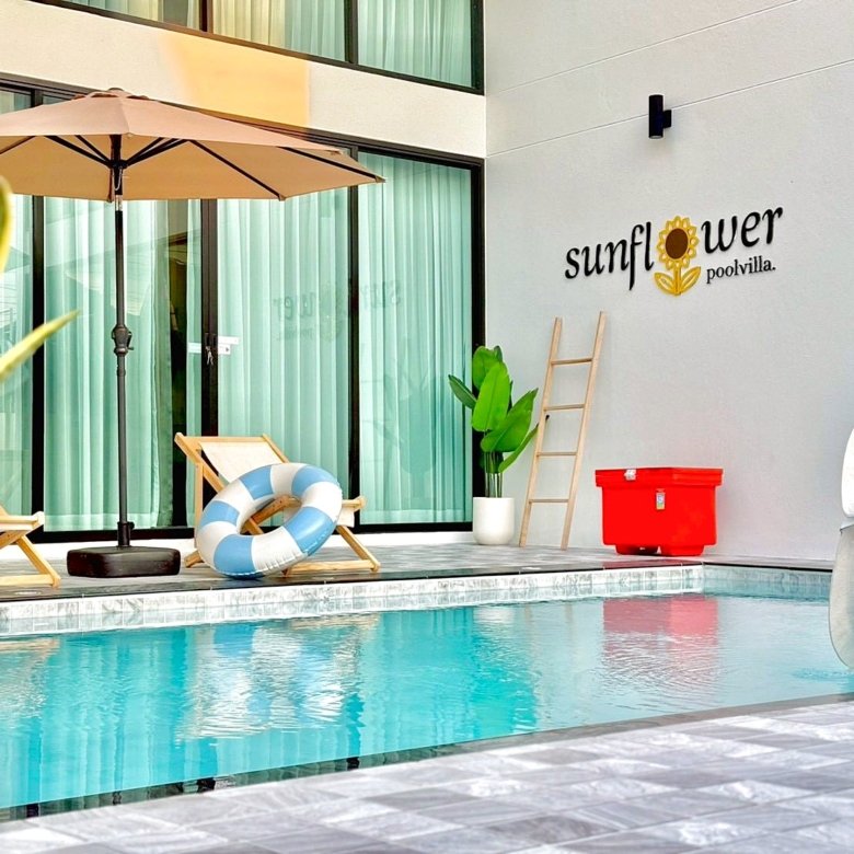 Poolside area at Sunflower Pool Villa two wooden lounge chairs a beige umbrella lifebuoy and a red cooler against a light wall