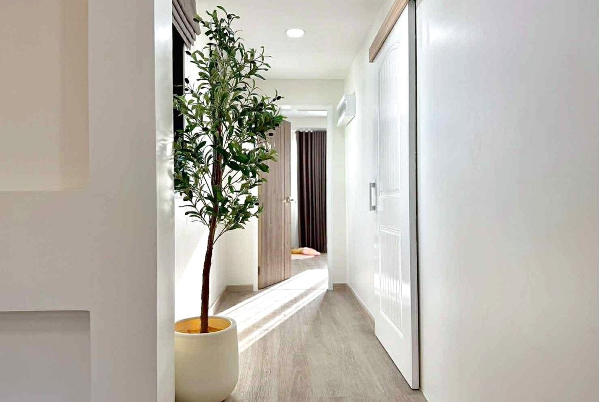 Bright, modern hallway with a tall potted plant on the left and an open door at the end leading to another room.