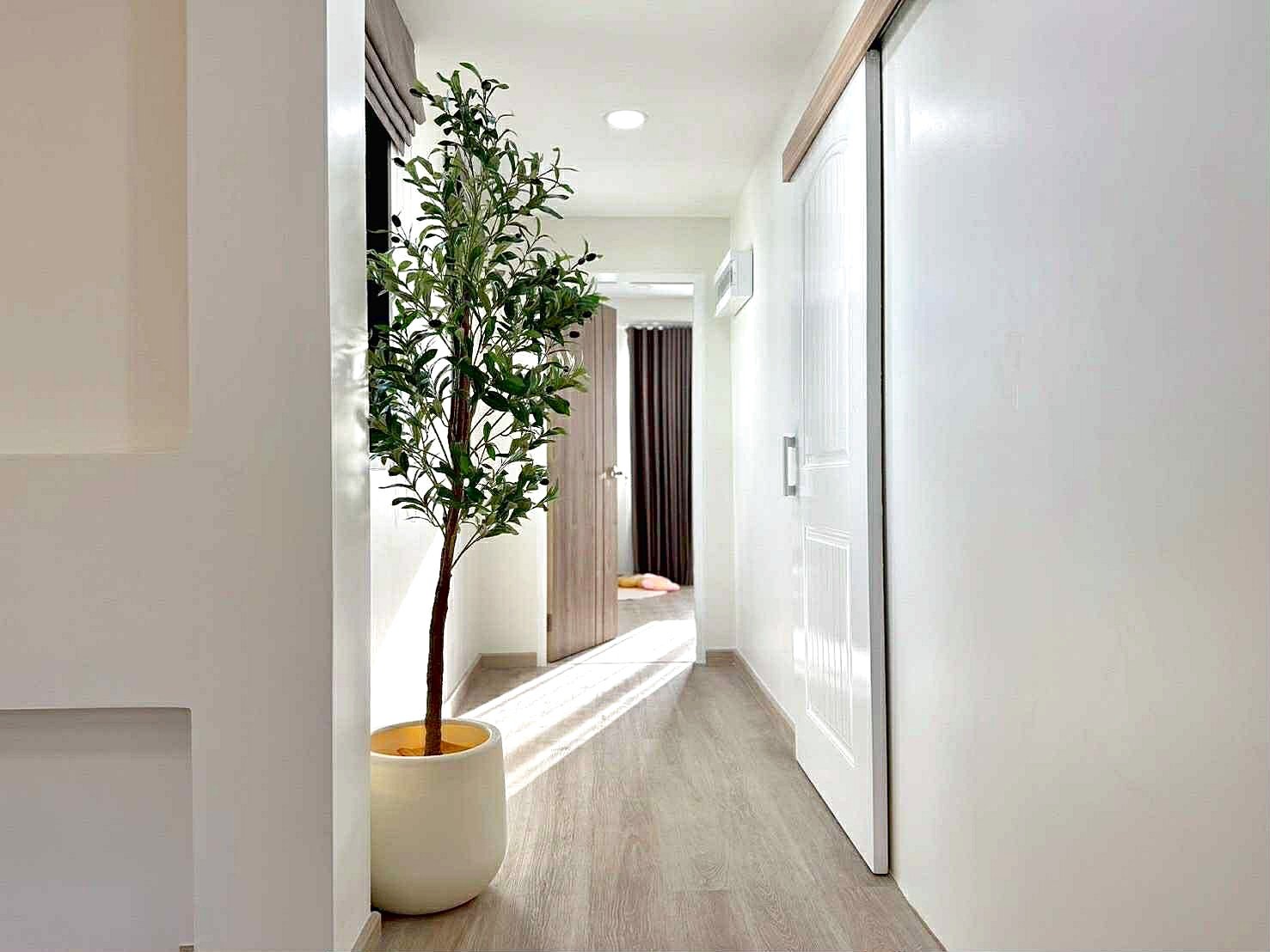 Sunflower_Pool_Villa_12 Bright, modern hallway with a tall potted plant on the left and an open door at the end leading to another room.