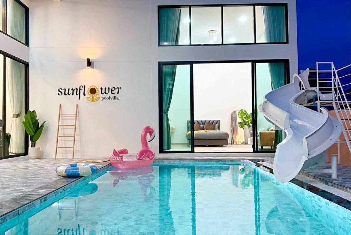Outdoor pool at Sunflower Pool Villa with a pink flamingo float, pool rings, ladder, and a white spiral slide beside glass doors opening to a living area.
