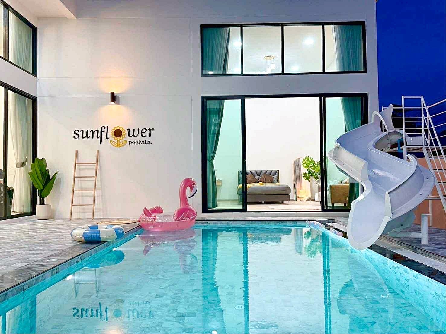 Sunflower_Pool_Villa_17 Outdoor pool at Sunflower Pool Villa with a pink flamingo float, pool rings, ladder, and a white spiral slide beside glass doors opening to a living area.