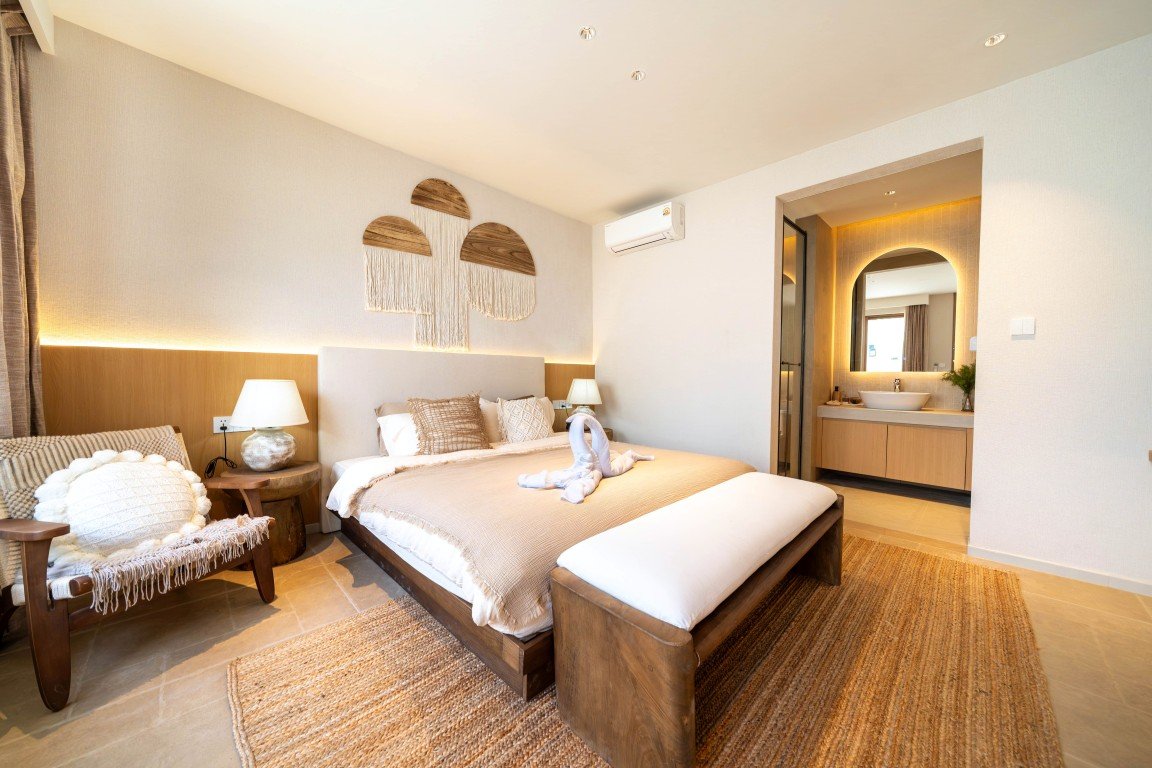 Hotel bedroom with a king bed, beige linens, wooden bench at foot, and a swan-towel sculpture on the bed.