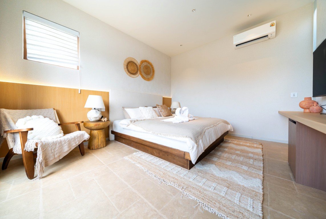 Hotel-like bedroom with a low wooden bed, neutral linens, and two woven wall decor pieces above the headboard.