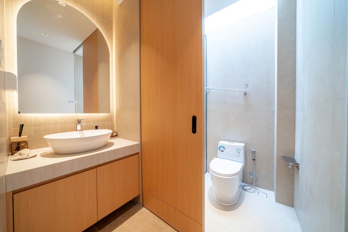 Modern bathroom with a wooden vanity, marble countertop, and a backlit arched mirror over a white vessel sink.