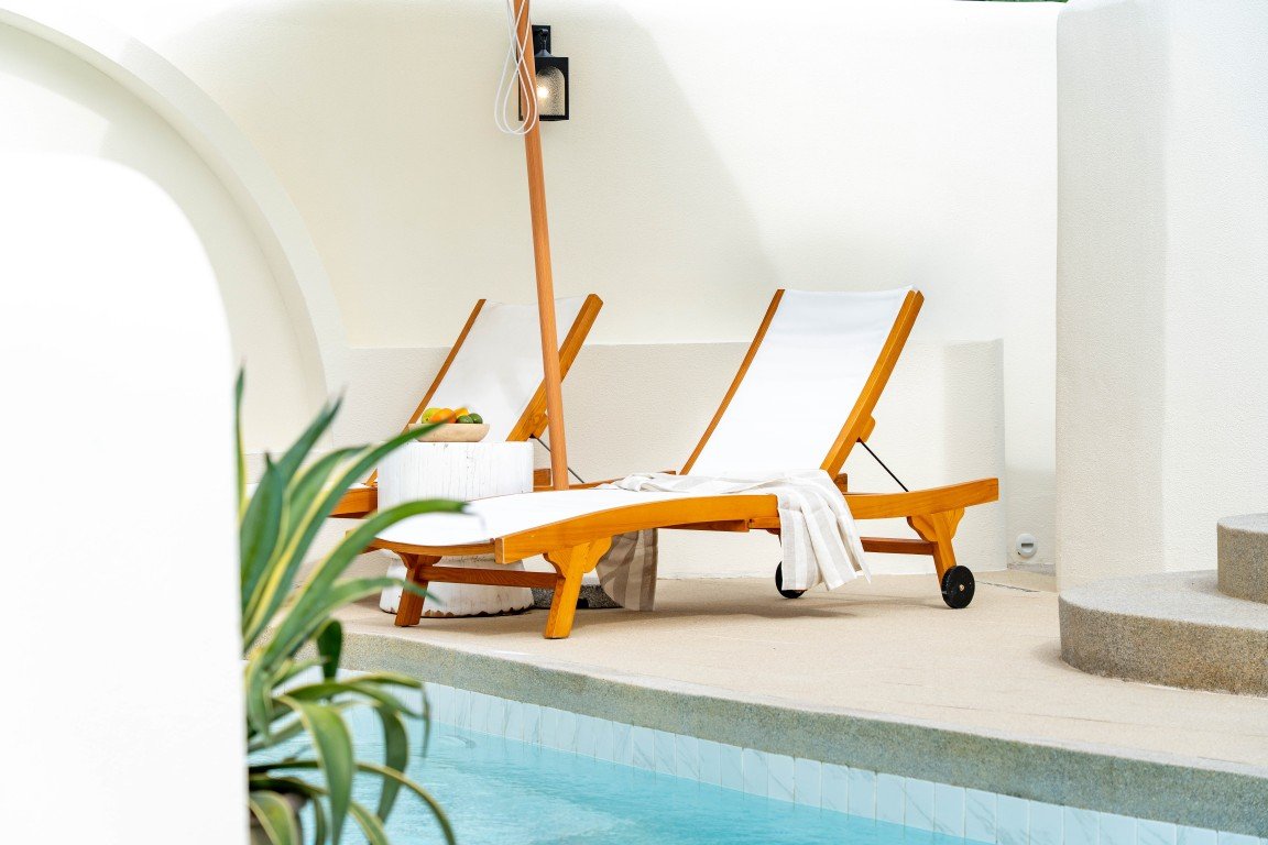 Two white fabric lounge chairs with wooden frames by a swimming pool, a towel draped over one chair.