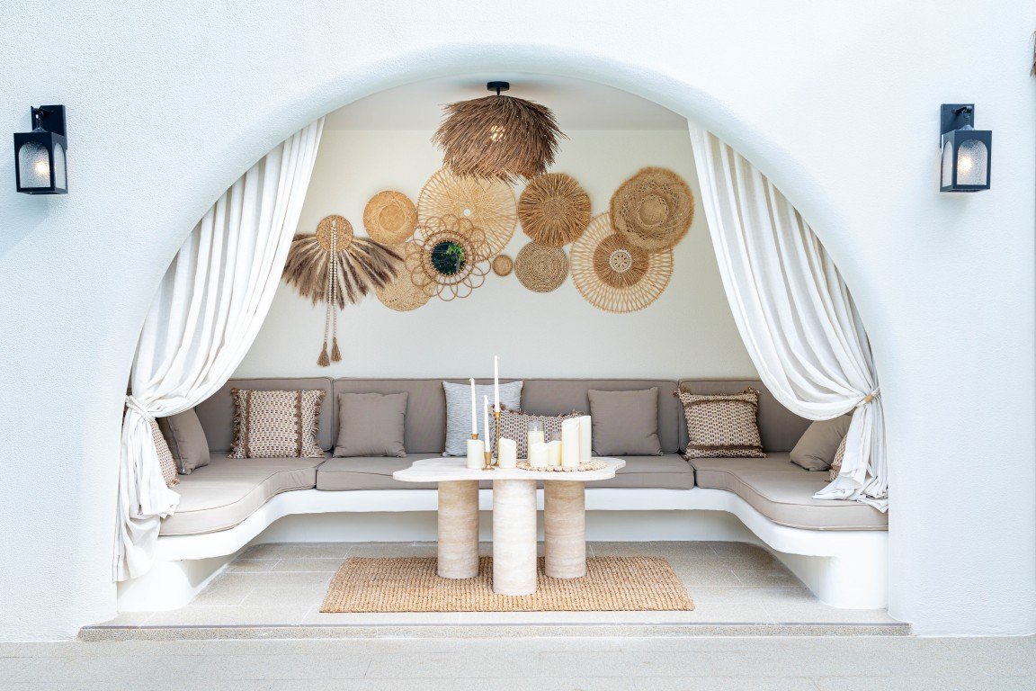 Cozy arched outdoor seating area with beige cushions, woven wall art, and a marble table with candles.