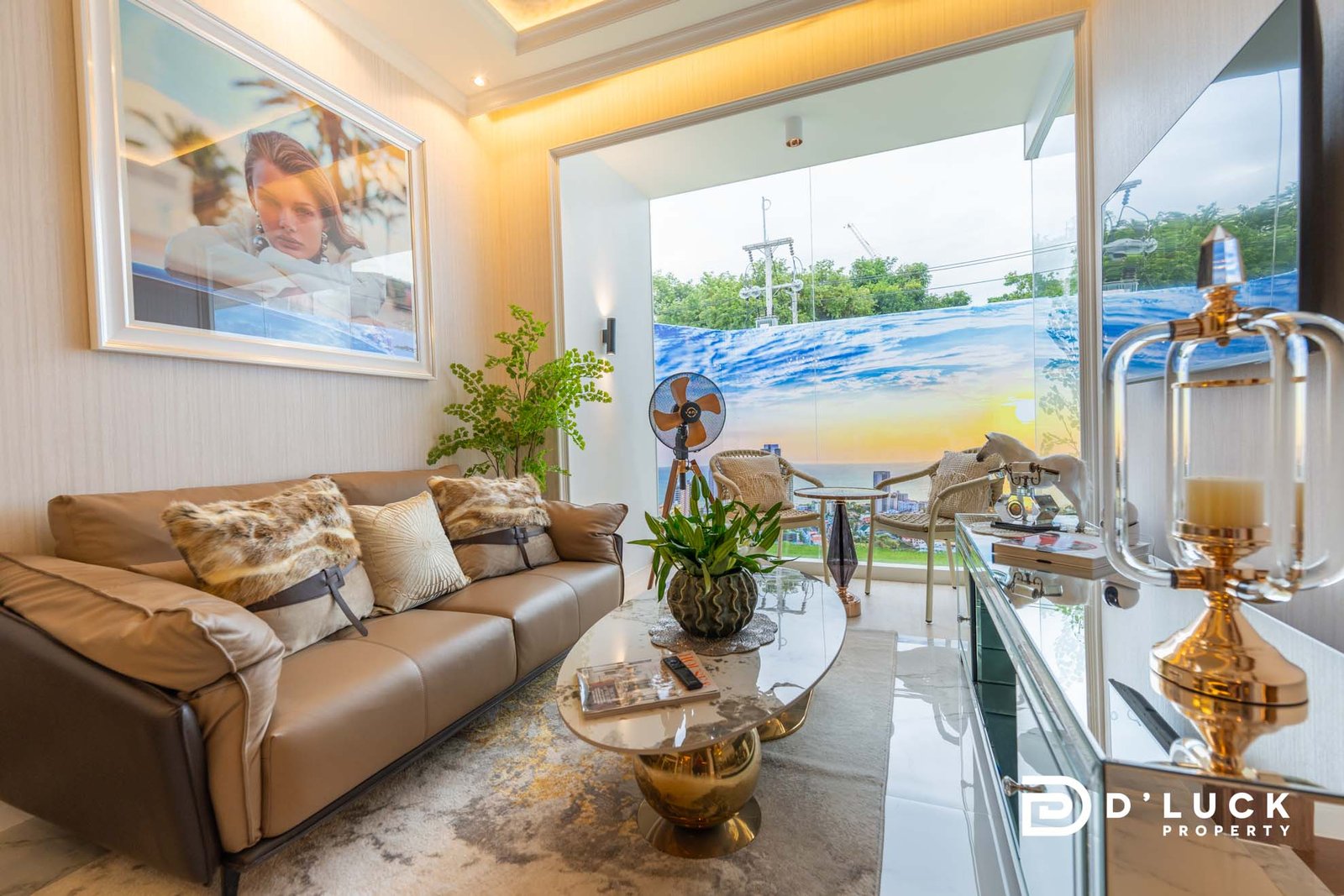The-Riviera-Malibu-1bedroom 1 Luxurious living room with a tan leather sofa, fluffy cushions, a marble coffee table, and a large window showing a coastal view.