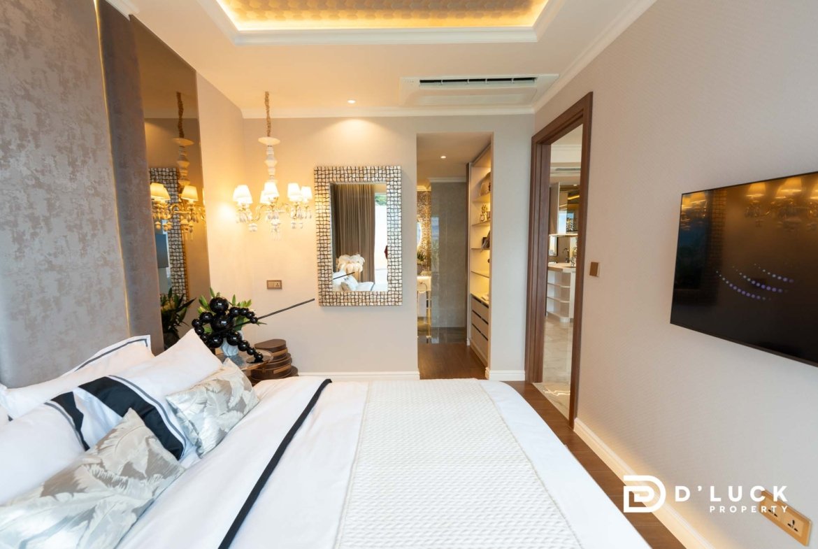 Luxurious hotel bedroom with white bedding, decorative pillows, and a chandelier-style light fixture.