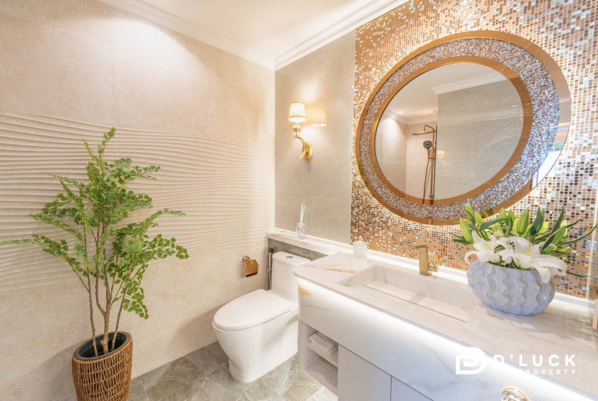 Hotel-style bathroom with a mosaic circular mirror, beige tiled walls, and a white vanity with a plant nearby.” But need not include quotes.