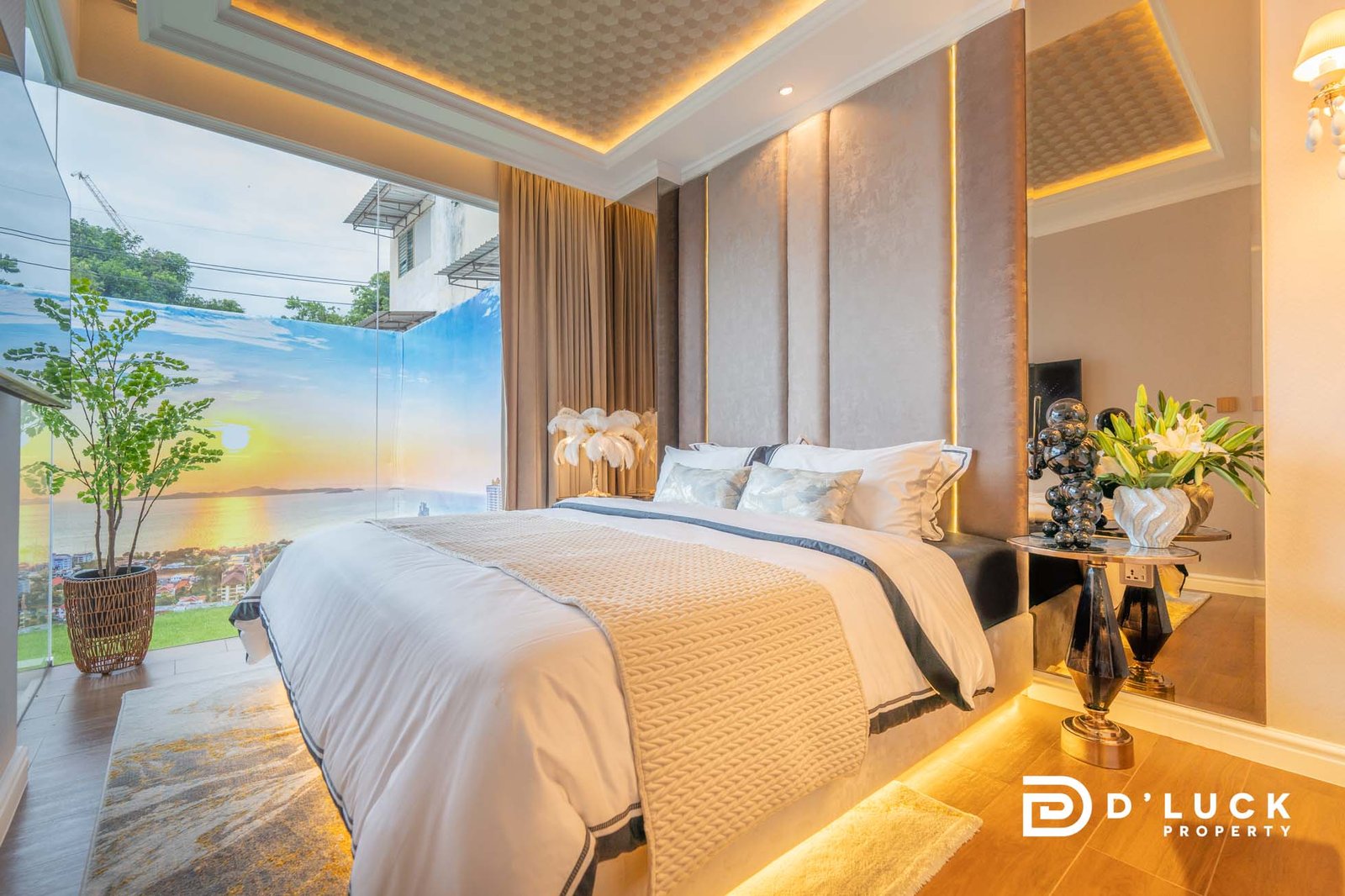 The-Riviera-Malibu-1bedroom 2 Luxurious bedroom with a large glass wall revealing a sunset by the ocean, king bed, neutral upholstered headboard, and warm ambient lighting.