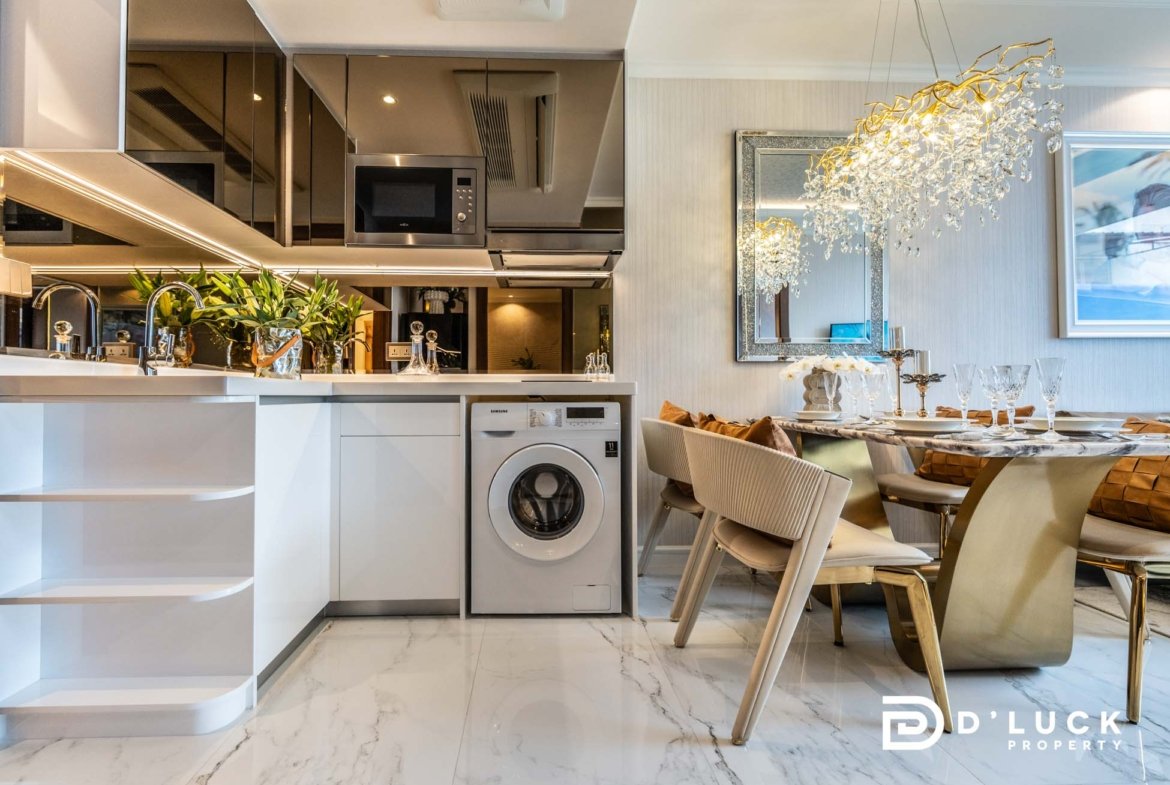Modern open-plan kitchen with stainless appliances, marble floor, and a glass chandelier over a dining table set with gold accents. Logo bottom right says 'Lucky Property'.