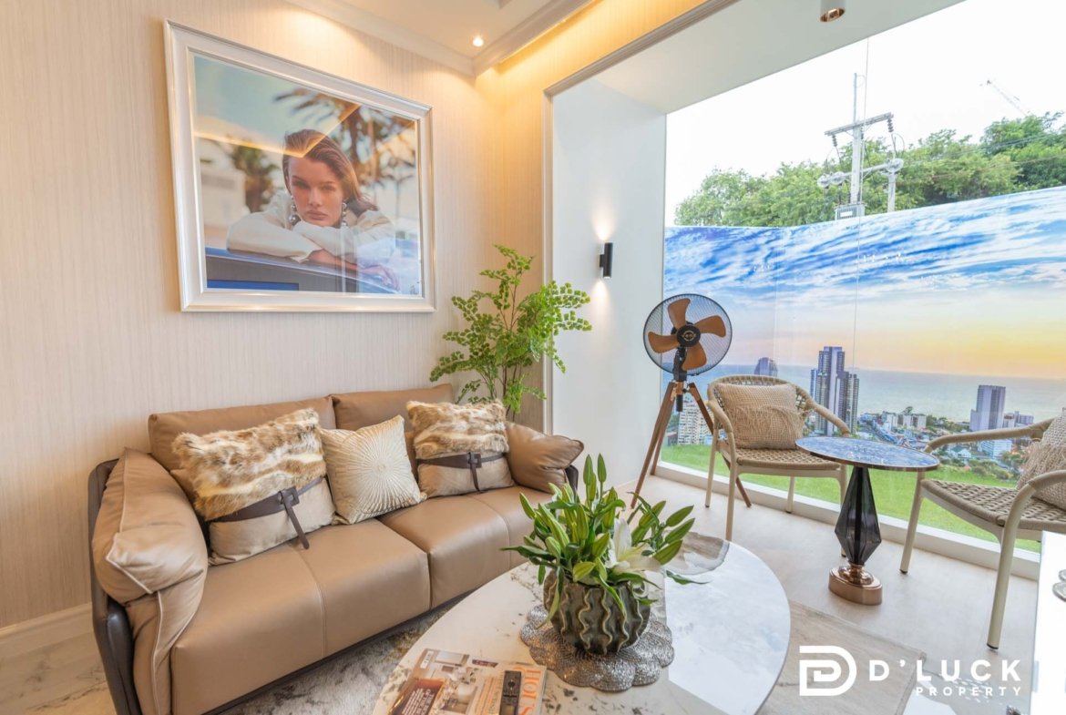 Modern living room with a beige leather sofa, fur cushions, and a glass coffee table; large window shows city skyline and ocean view.