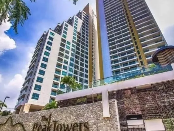 Two tall modern residential towers with blue glass windows rise above a stone-front entrance, palm trees nearby, under a bright blue sky.”,