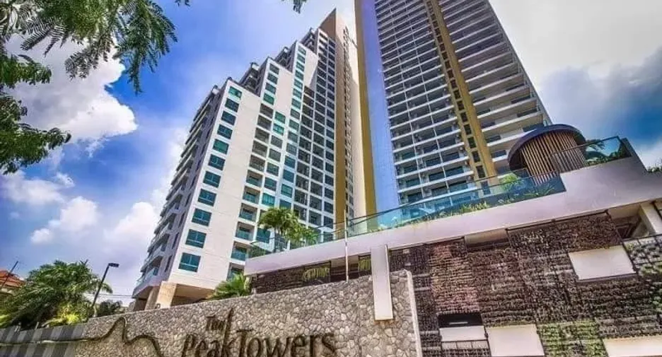 Two tall modern residential towers with blue glass windows rise above a stone front entrance palm trees nearby under a bright blue sky