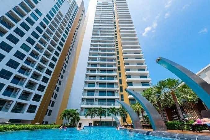 Tall modern high-rise condo with a swimming pool at the base, blue sculpture arches, and palm trees under a clear sky.