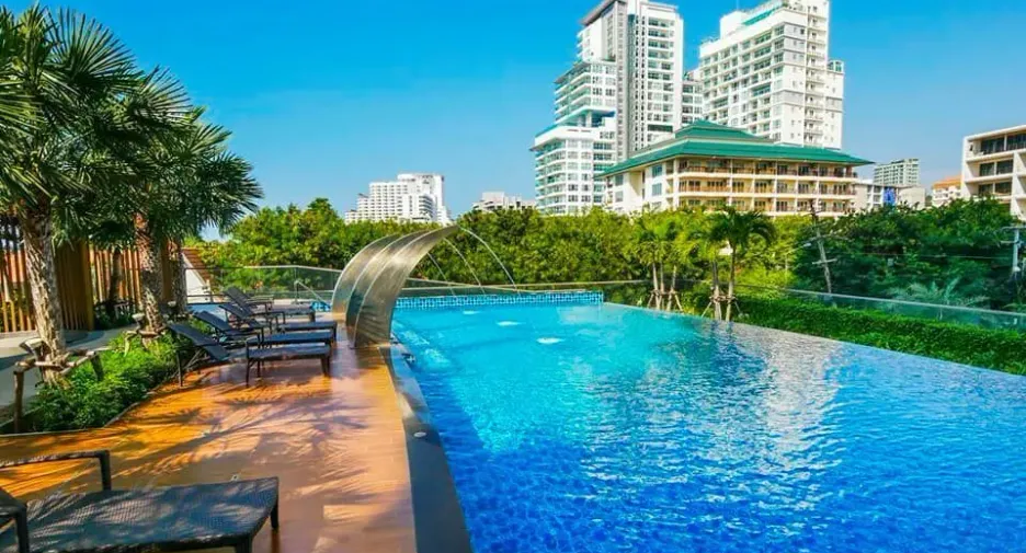 Infinity pool at a resort with blue water, lounge chairs, palm trees, and high-rise buildings in the background.