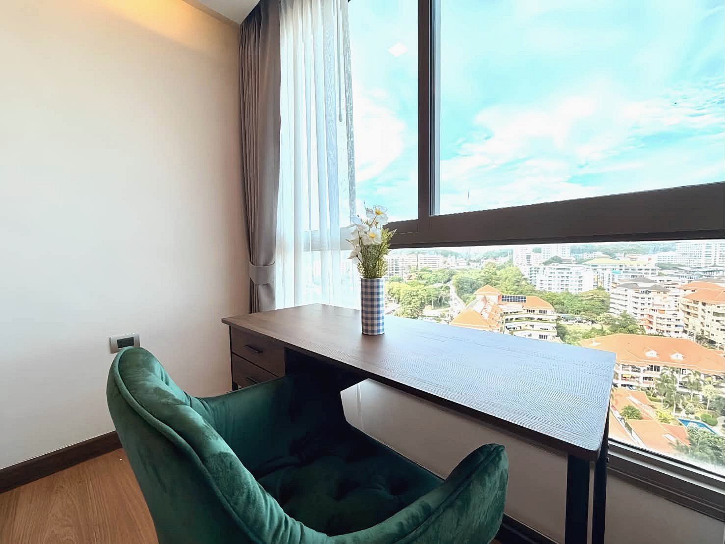 The_Peak_Tower_Rent_Rdl340_10 Home office corner with a dark wooden desk, green velvet chair, and a vase of flowers near a large window overlooking a cityscape.