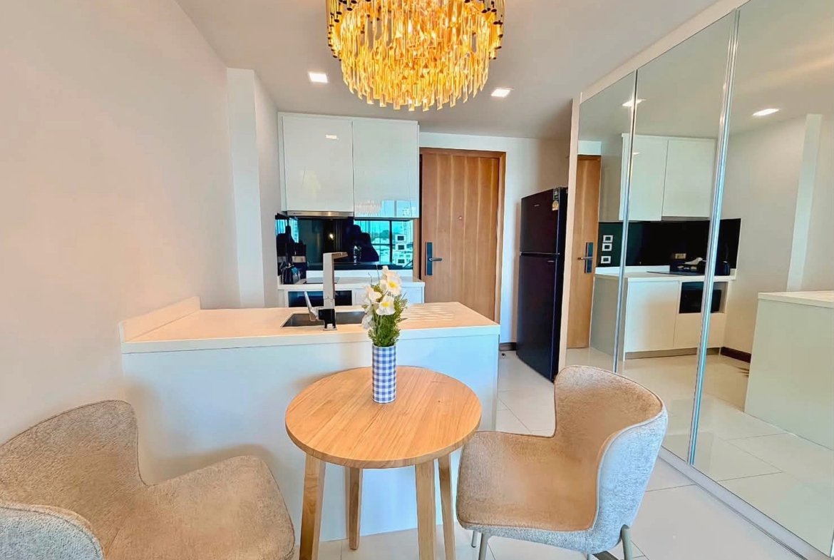 Modern kitchen with a white island, round wooden table with a flower vase, and a gold chandelier overhead.