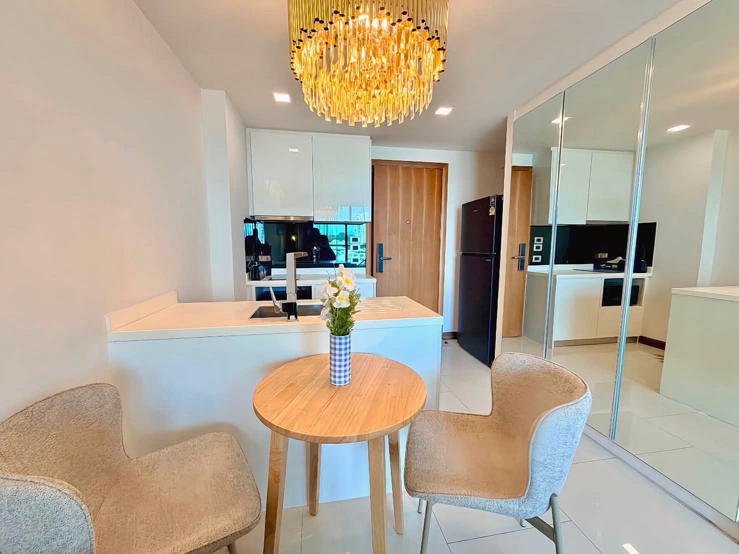 The_Peak_Tower_Rent_Rdl340_14 Modern kitchen with a white island, round wooden table with a flower vase, and a gold chandelier overhead.