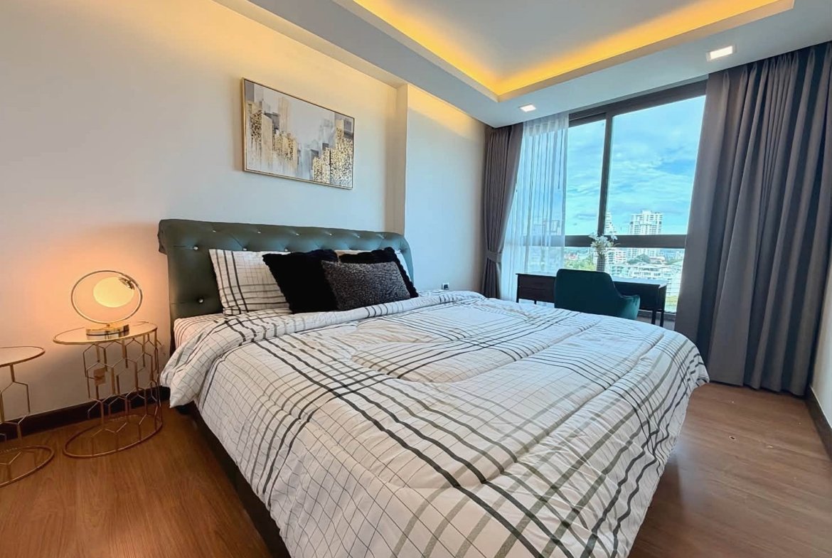 Hotel bedroom with a king bed, green tufted headboard, plaid bedding, and round gold nightstands with lamps on each side.