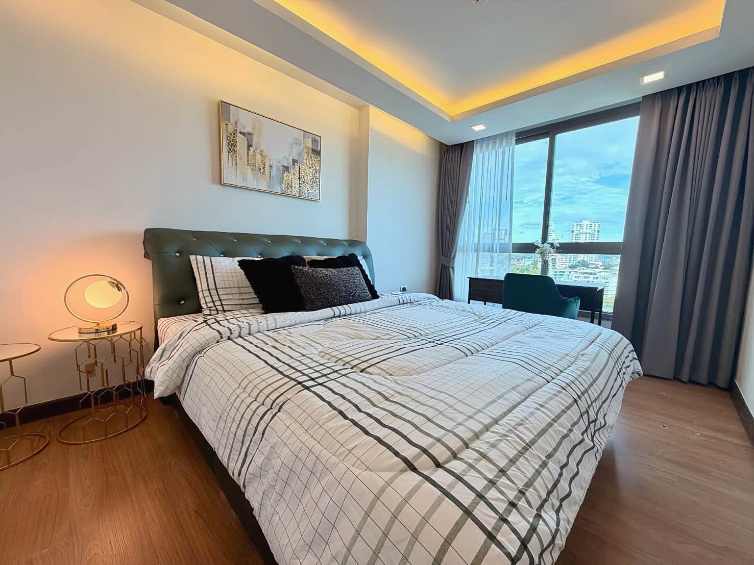 The_Peak_Tower_Rent_Rdl340_3 Hotel bedroom with a king bed, green tufted headboard, plaid bedding, and round gold nightstands with lamps on each side.