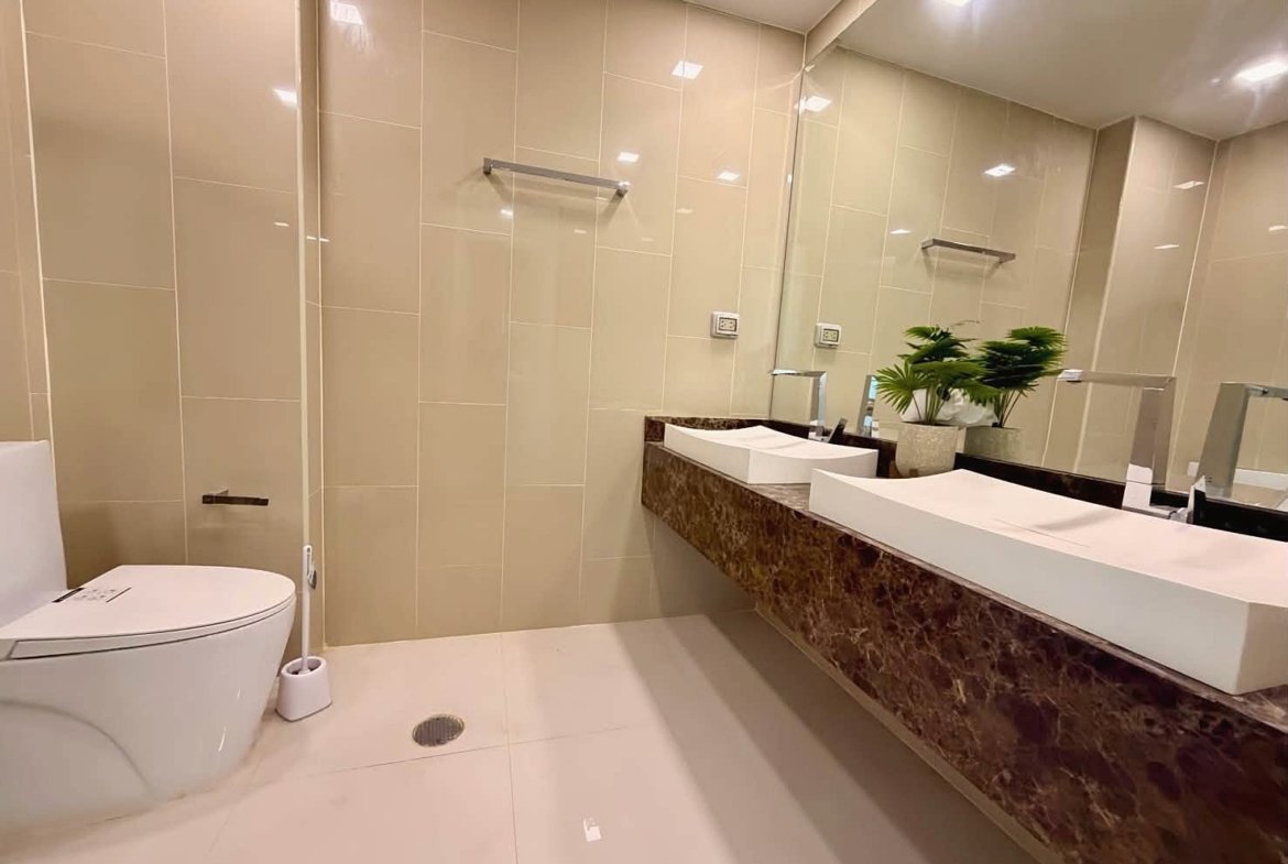 Modern bathroom with beige tile walls, a long brown marble countertop, and two rectangular under-mount sinks with a large mirror above.