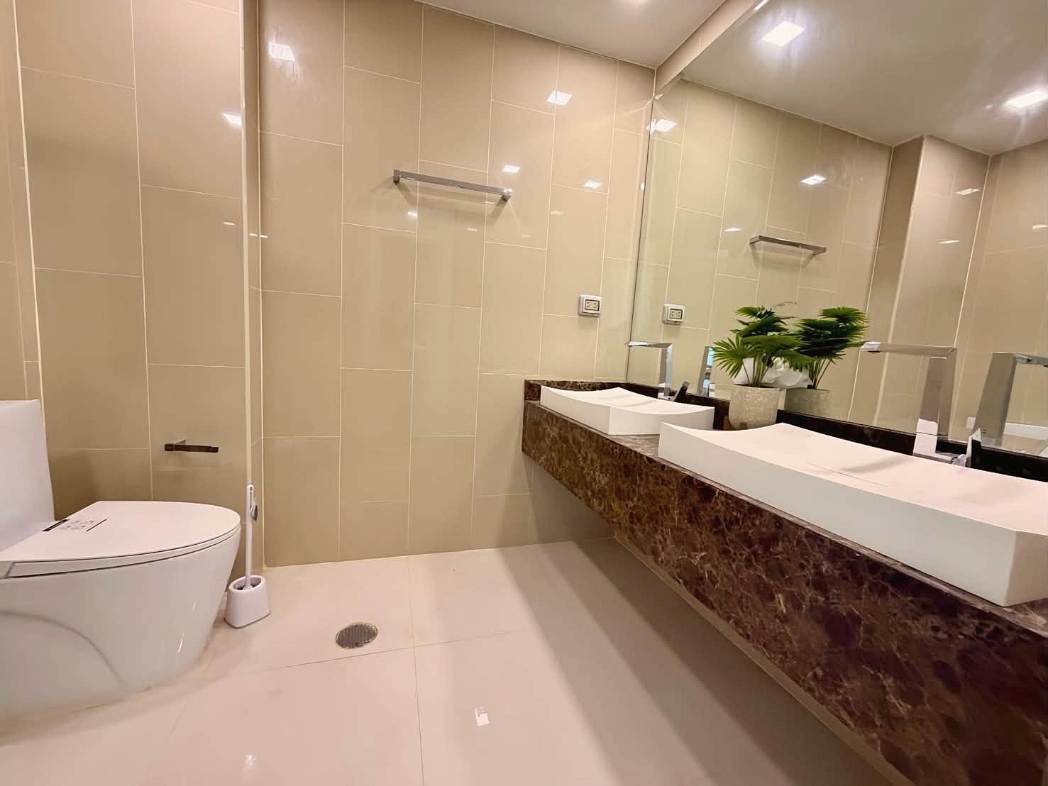 The_Peak_Tower_Rent_Rdl340_9 Modern bathroom with beige tile walls, a long brown marble countertop, and two rectangular under-mount sinks with a large mirror above.