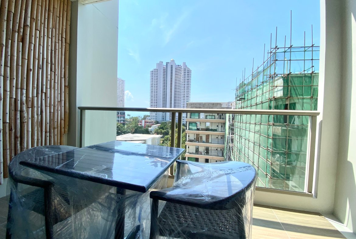 Indoor balcony with plastic-covered tables and chairs, view of city buildings through a large window and construction scaffold on the right
