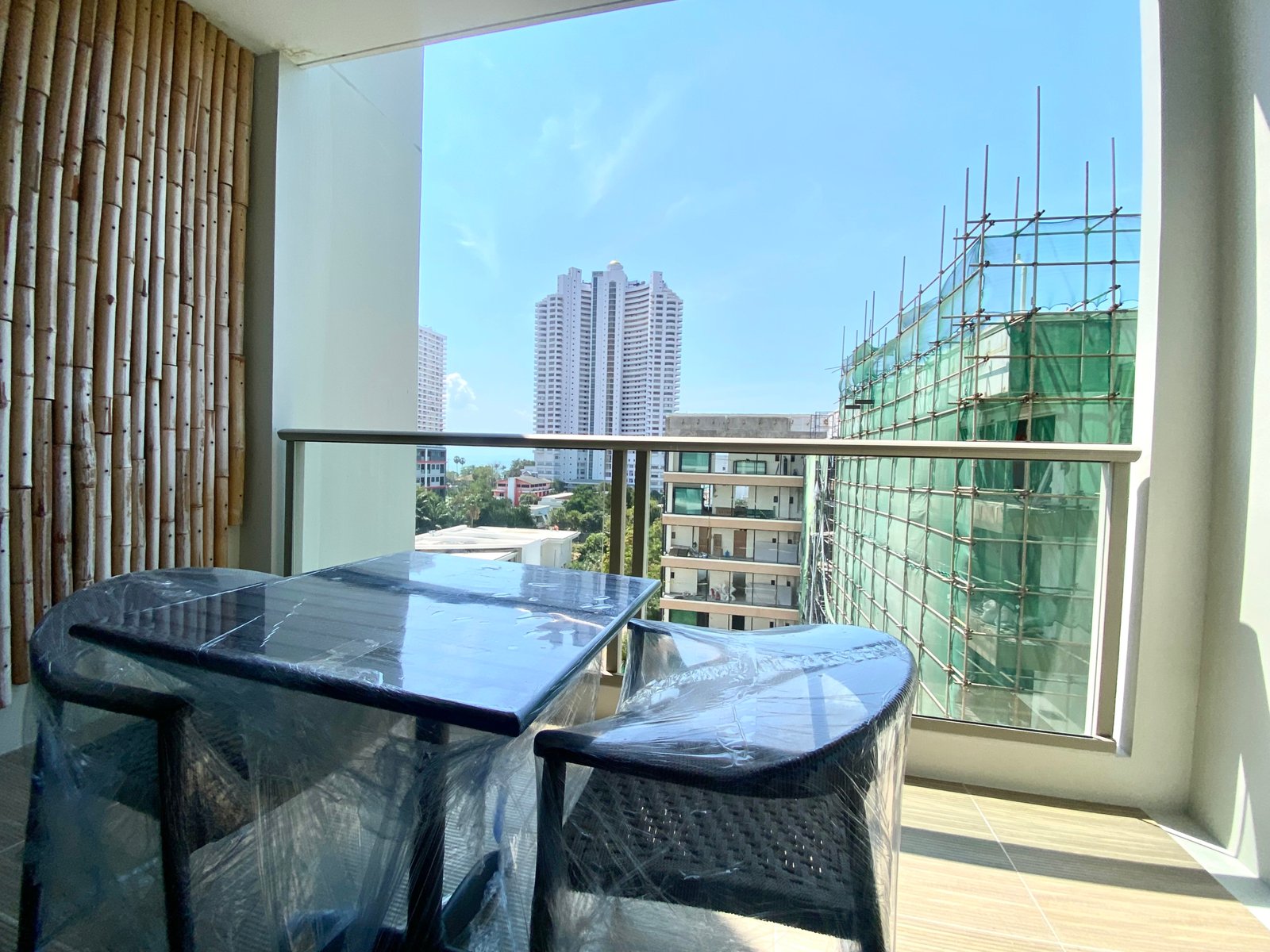 Indoor balcony with plastic-covered tables and chairs, view of city buildings through a large window and construction scaffold on the right
