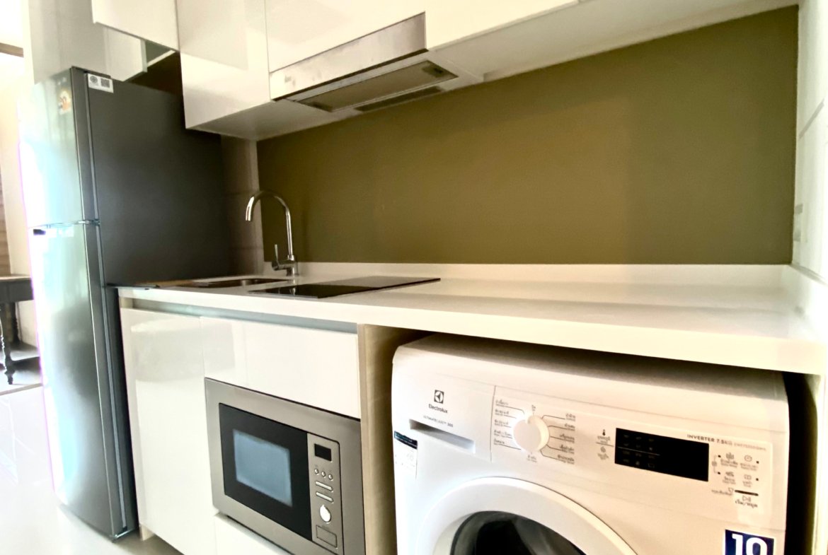 Modern white kitchen with tall gloss cabinets, a built-in oven and microwave, and a front-loading washing machine beneath the counter.