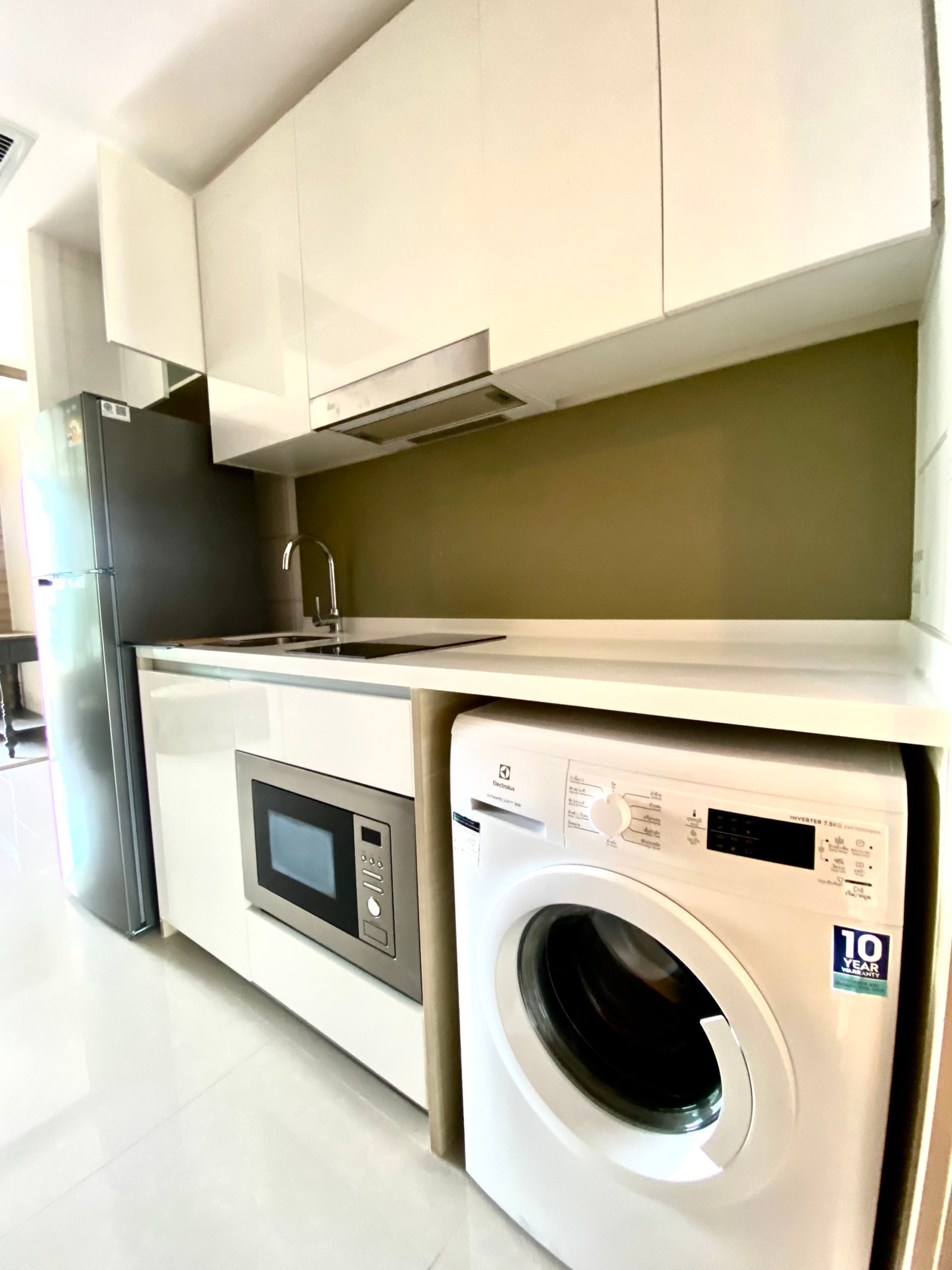 Modern white kitchen with tall gloss cabinets, a built-in oven and microwave, and a front-loading washing machine beneath the counter.