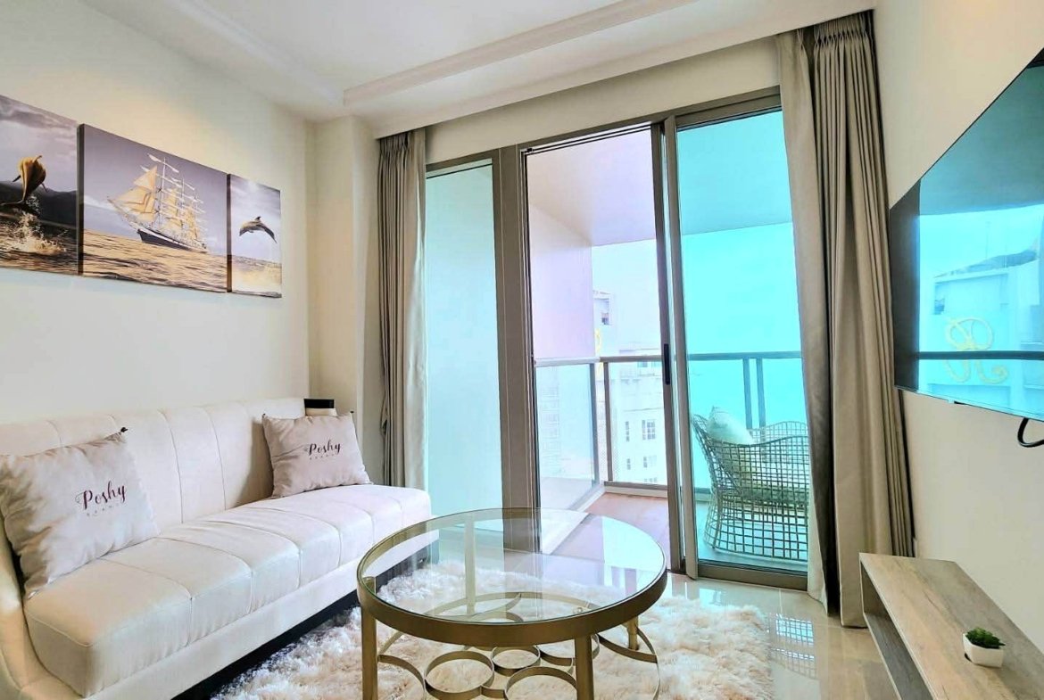 Bright modern living room with a white sofa, glass coffee table, and a three-panel ship artwork above the couch.