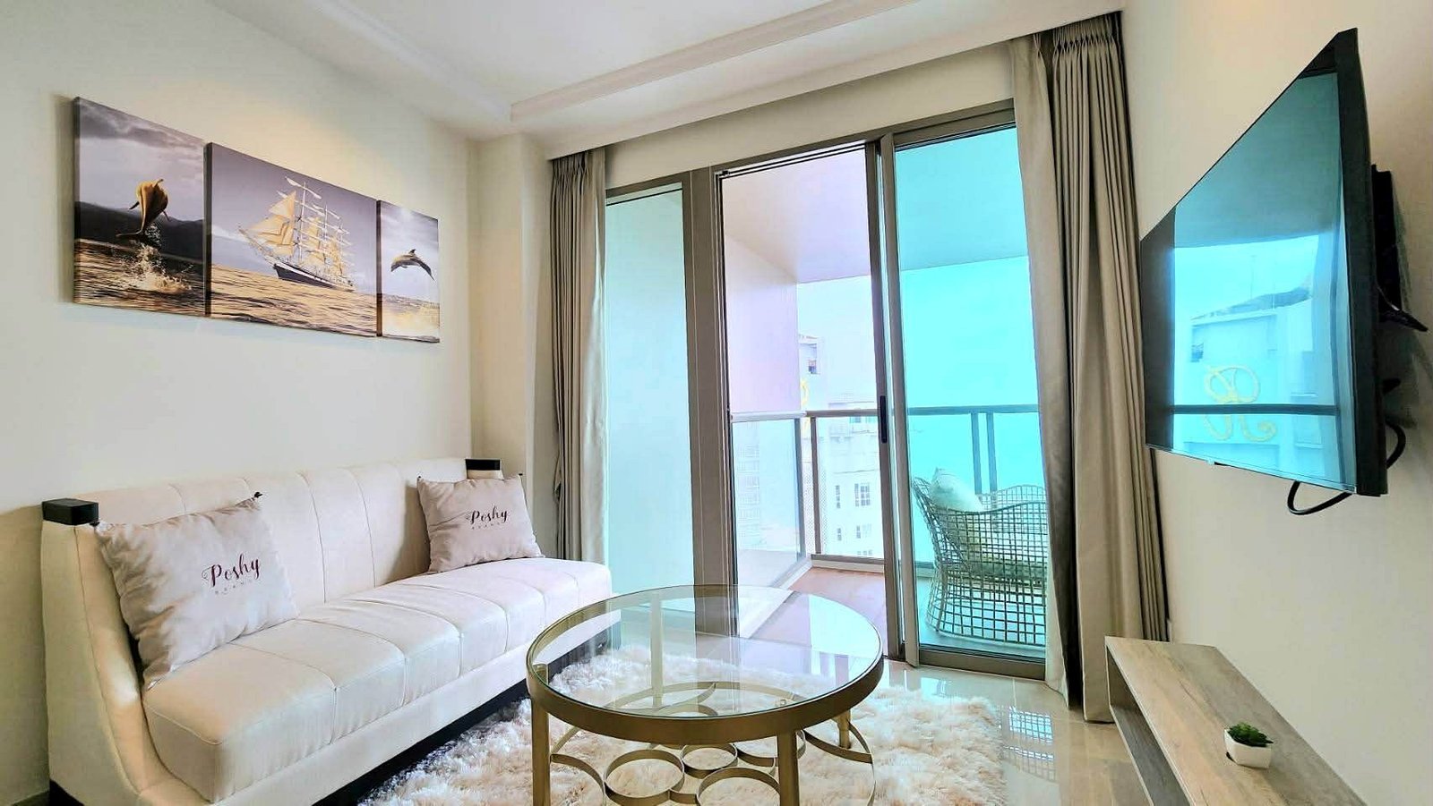 Bright modern living room with a white sofa, glass coffee table, and a three-panel ship artwork above the couch.