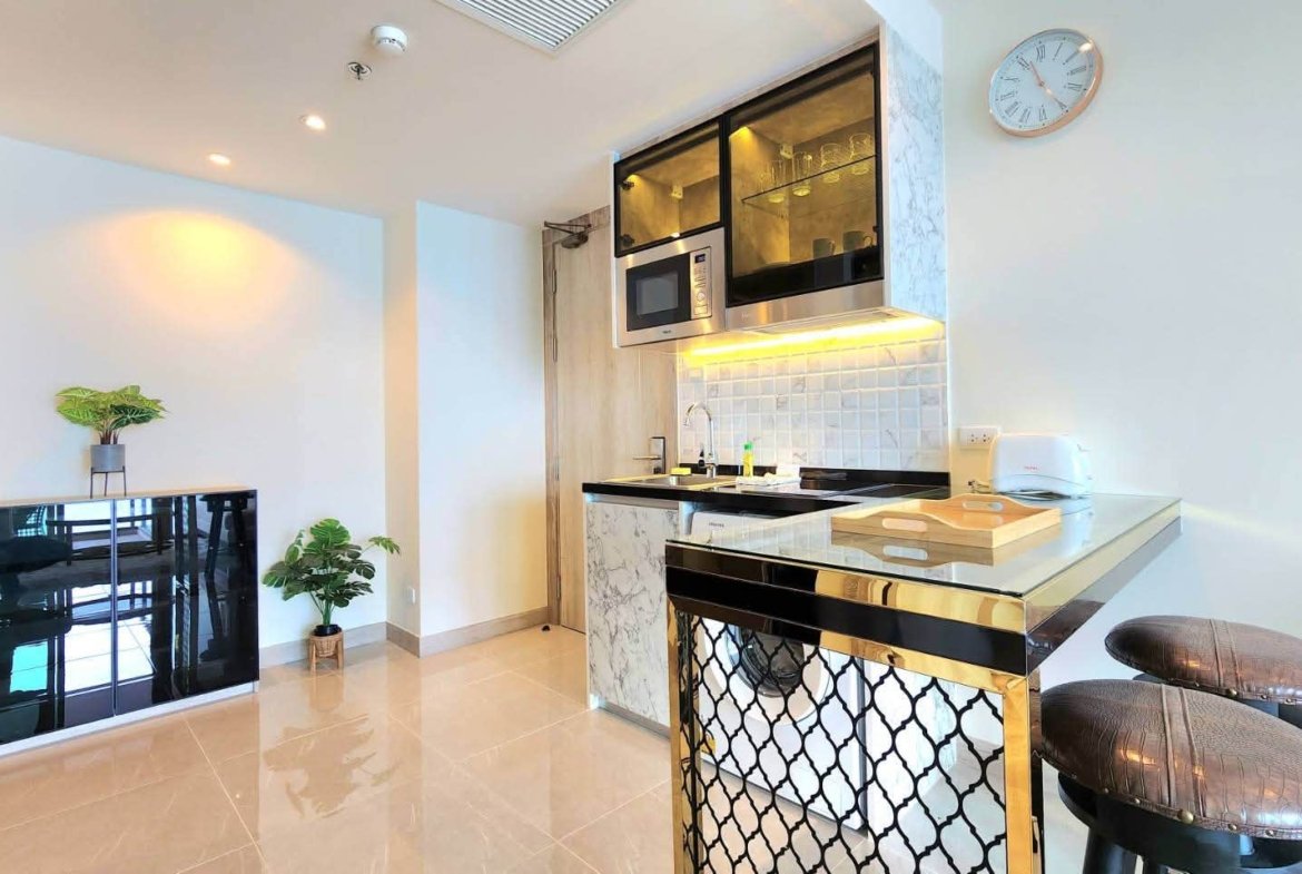 Modern kitchen with marble island, black glass-front cabinets, and stainless-steel microwave/oven; two cushioned bar stools at a gold-and-black counter.