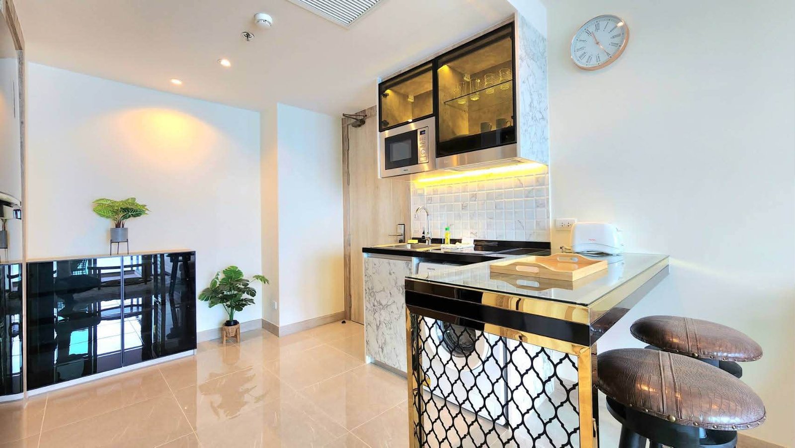 Modern kitchen with marble island, black glass-front cabinets, and stainless-steel microwave/oven; two cushioned bar stools at a gold-and-black counter.