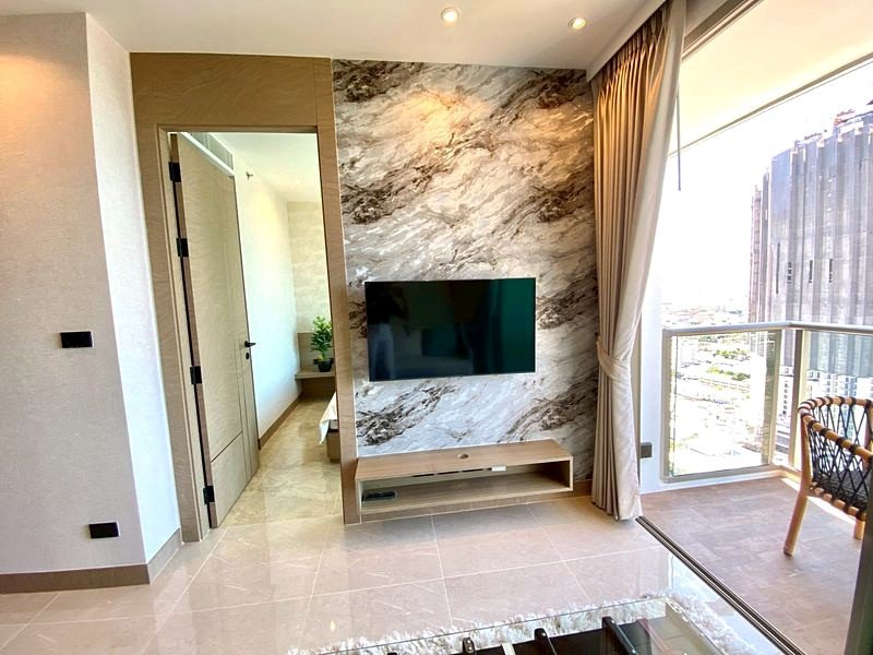 Living room with a marble feature wall behind a wall-mounted TV and a wooden media console; glass balcony door nearby with curtains.