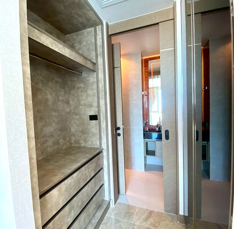 Walk-in closet with beige marble drawers and open shelves, leading to a bathroom with mirrored doors.