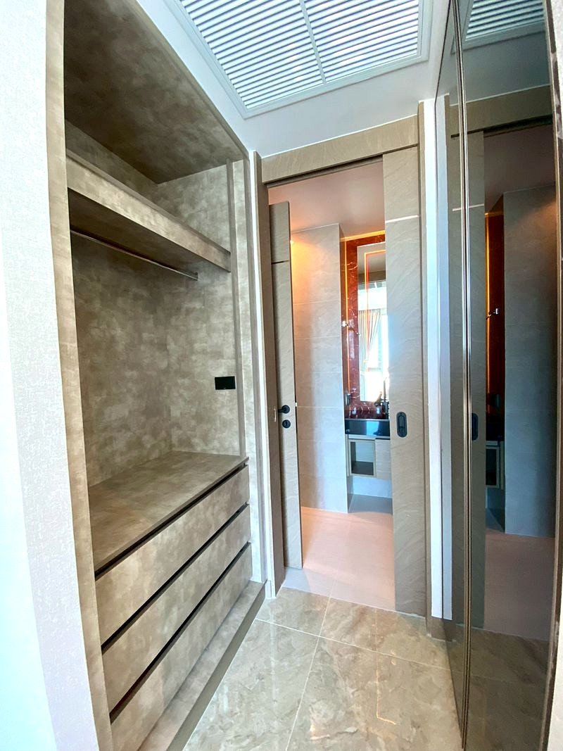 The_Riviera_Ocean_Drive_3014_6 Walk-in closet with beige marble drawers and open shelves, leading to a bathroom with mirrored doors.