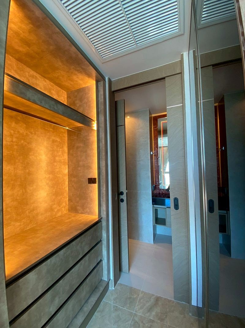 The_Riviera_Ocean_Drive_3014_7 Warmly lit built-in cabinet with open storage and drawers along a beige wall, in a modern bathroom/closet area.