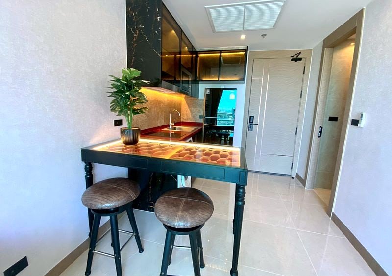 Compact kitchen with a dark high table, two round tufted stools, and a potted plant by the wall-mounted cabinets.