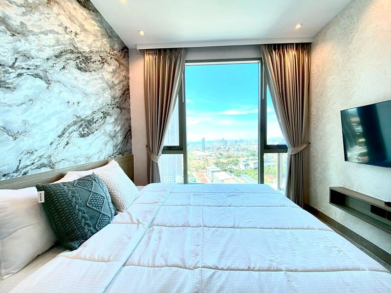 Hotel room with a large window view of the city skyline, bed in foreground and neutral decor.