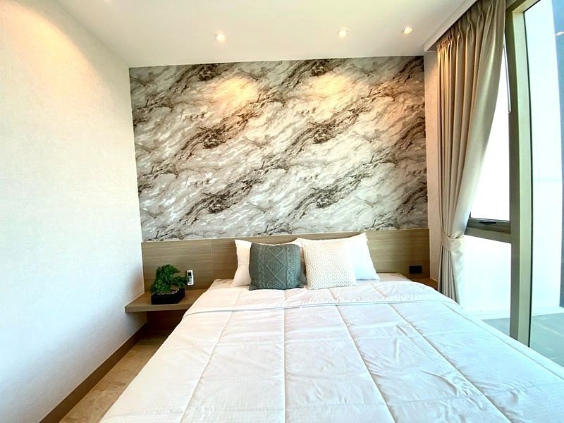 Bedroom with a marble accent wall behind a neatly made bed and a small plant on a floating nightstand