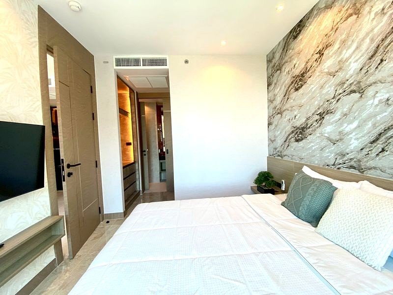 Hotel room with a large bed, white bedding and teal pillows, marble accent wall, and a doorway to the bathroom area on the left.